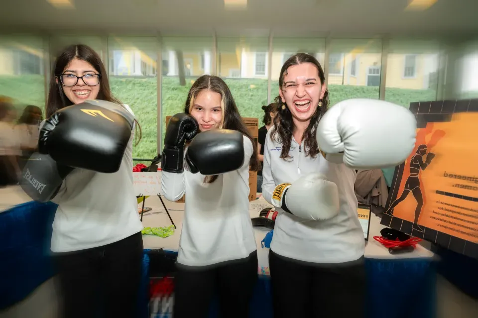 Three students hold up boxing gloves to the camera